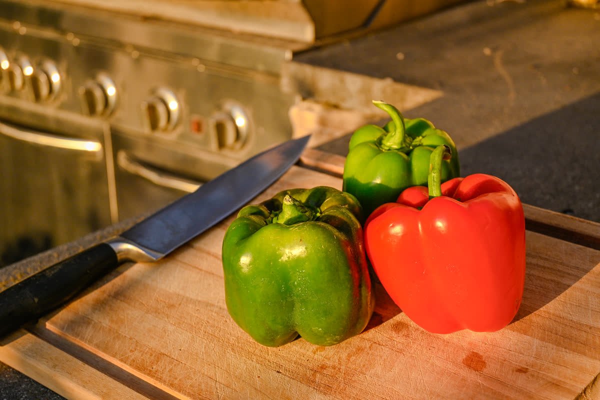 Red and green bell peppers on a cutting board in evening light