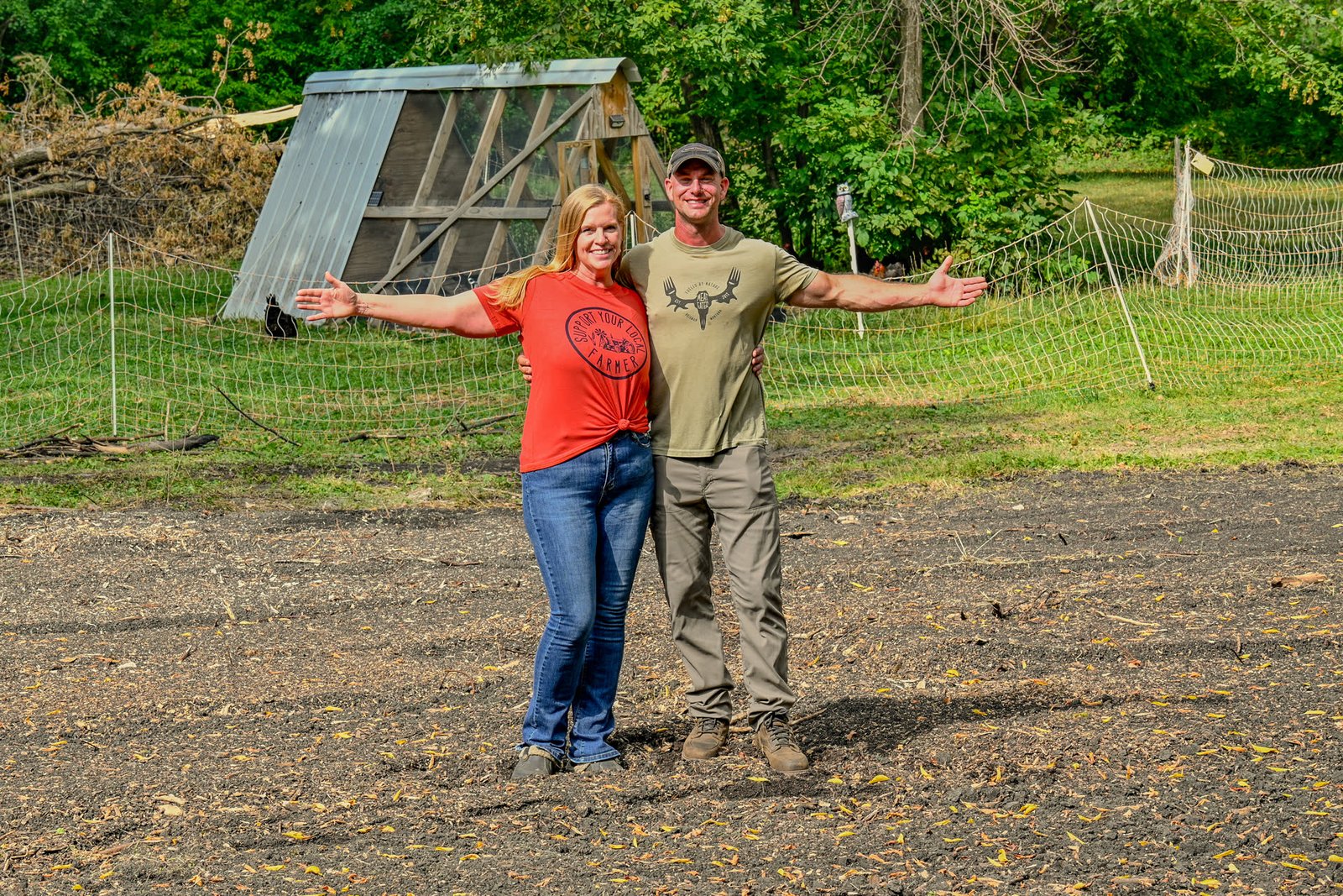 Drew and Sorell standing with arms outstretched in front of a coop on their newly prepared field