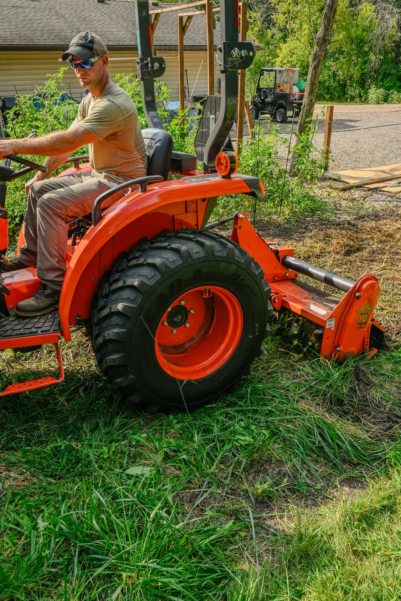 Farmer on an orange compact tractor working new ground with a rotary tiller